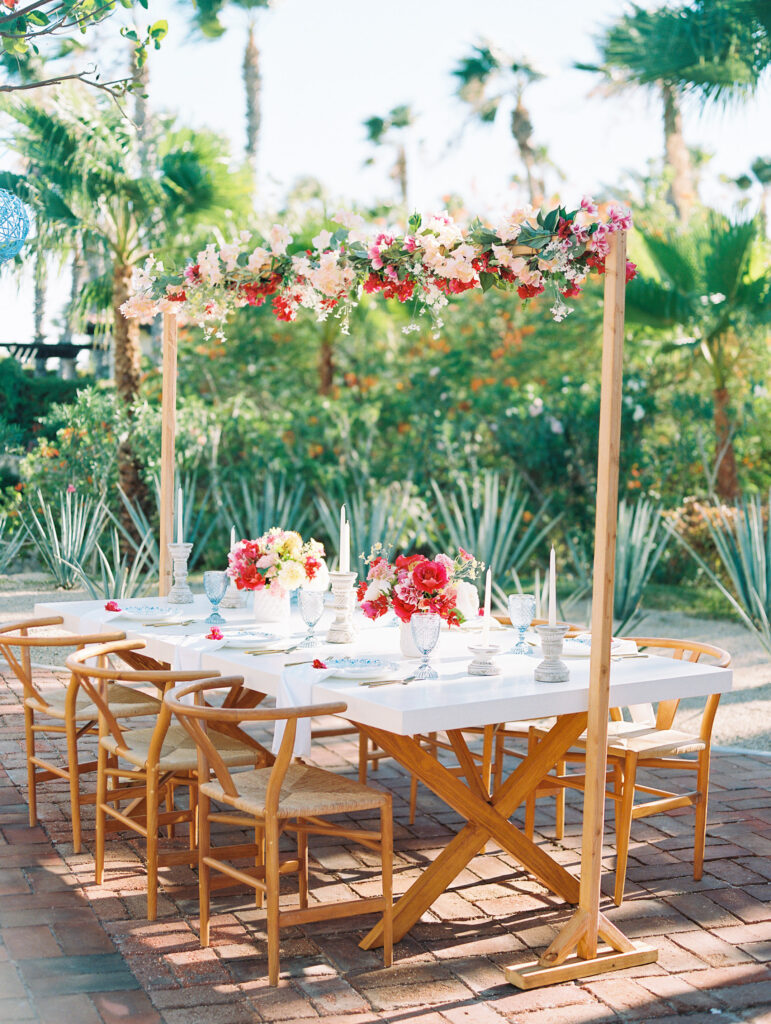 Colorful dinner table with hot pink flowers arrangements on top and hanging overhead