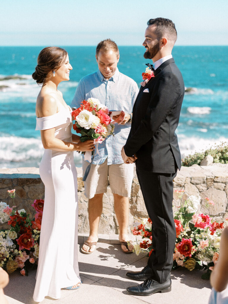 Man and woman getting married in front of the ocean with colorful flowers