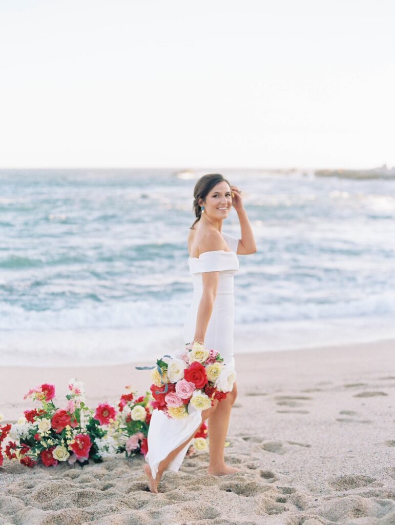 Bride walking on beach with colorful wedding flowers.