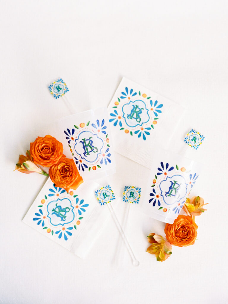 Fun custom orange and blue bar napkins, cups, and drink stirrers with vibrant orange florals 