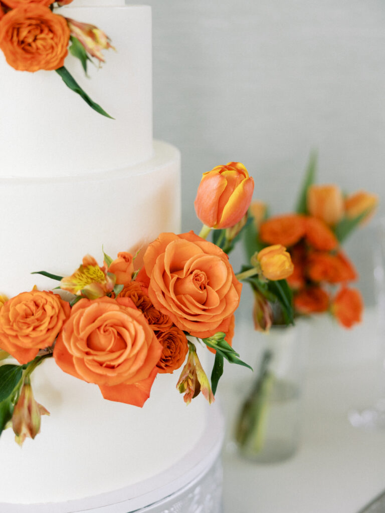 White wedding cake decorated with vibrant orange florals including roses and tulips