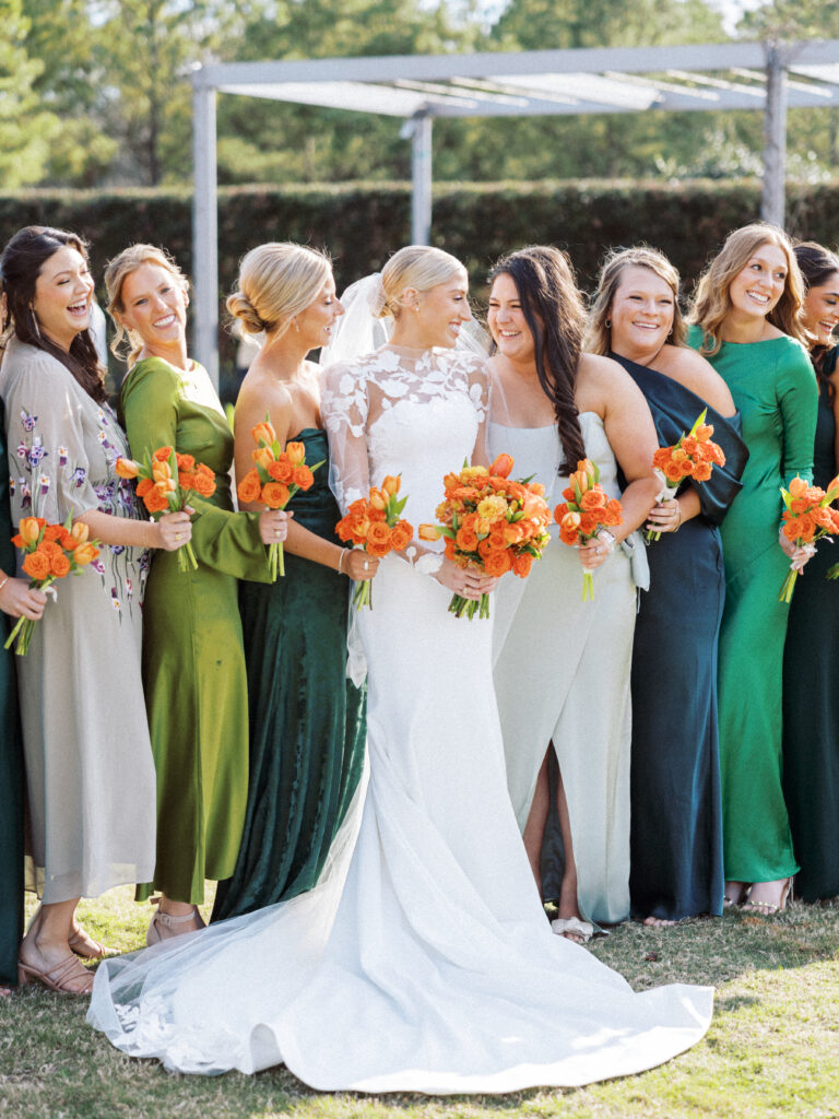 Bride with her bridesmaids wearing various shades of green dresses all holding bouquets made up of orange flowers