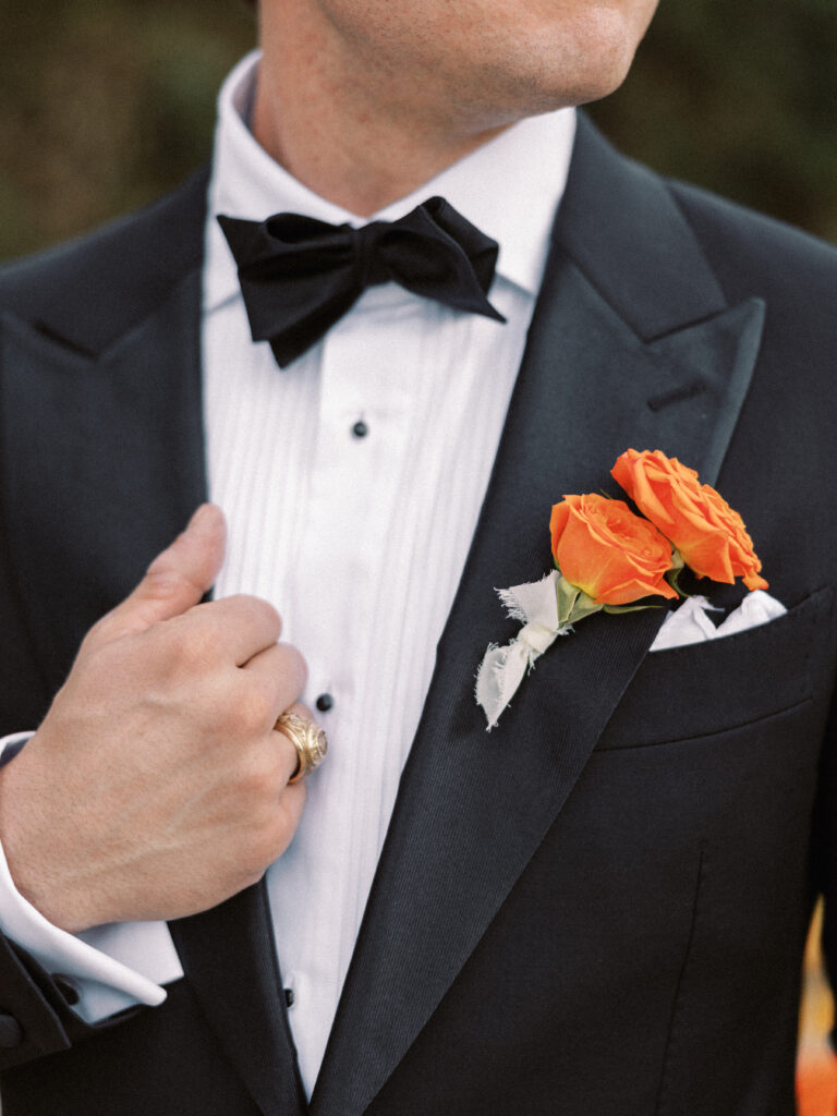 A boutonniere made with orange spray roses pinned on the groom for his wedding day