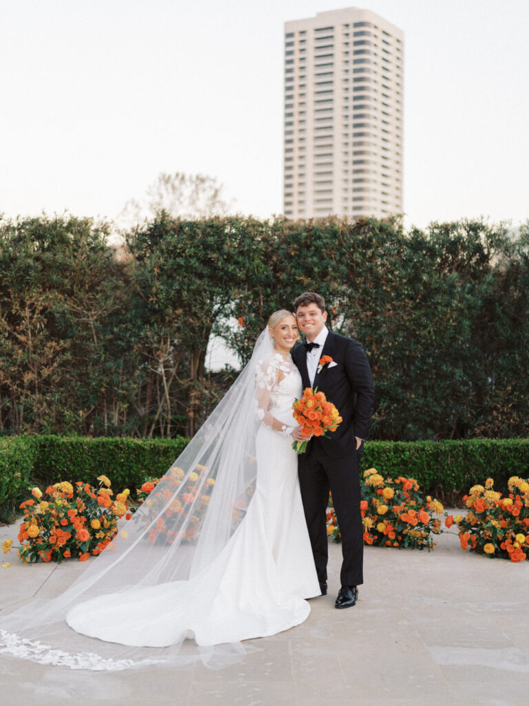 An outdoor wedding ceremony set up with bride and groom standing at the alter surrounded by a semi circle of orange flower arrangements