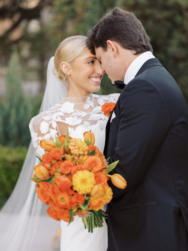 Bride and groom posing during wedding day with the bridal bouquet made with bright and vibrant orange flowers 