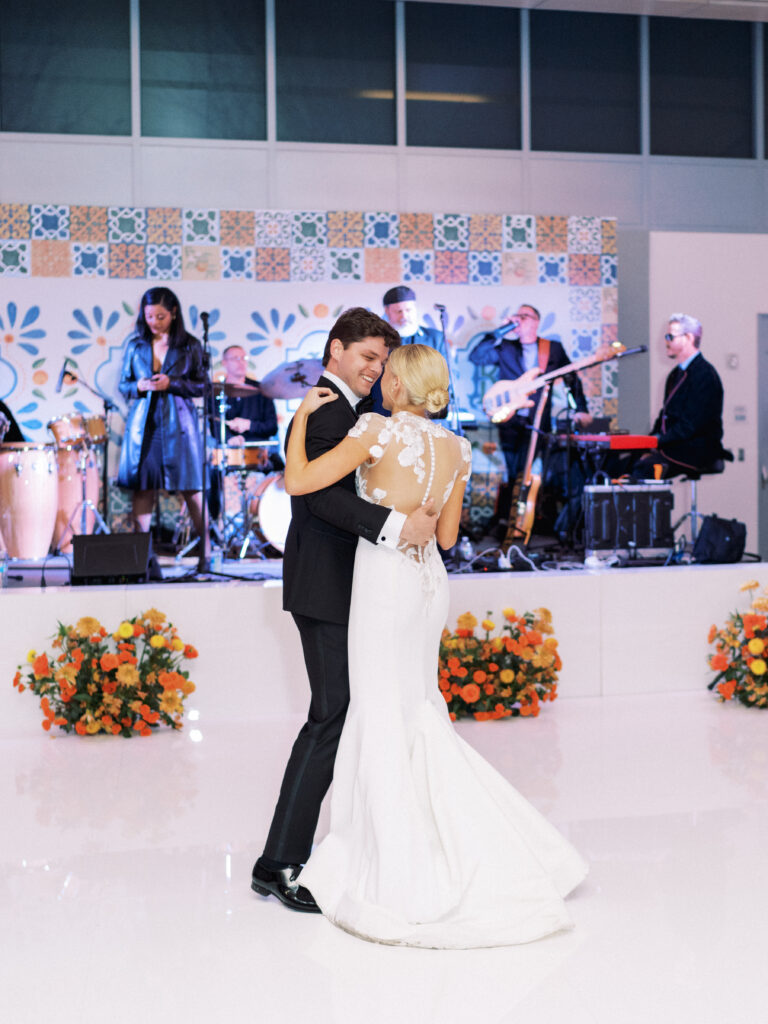 Bride and groom dancing in front of custom stage with orange floral arrangements lining the front during wedding reception 