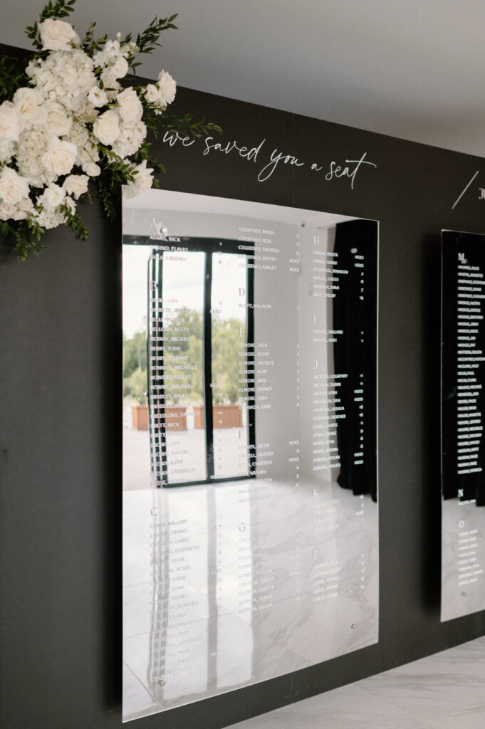 A modern floral arrangement made of all white flowers placed on the top corner of the mirrored seating chart