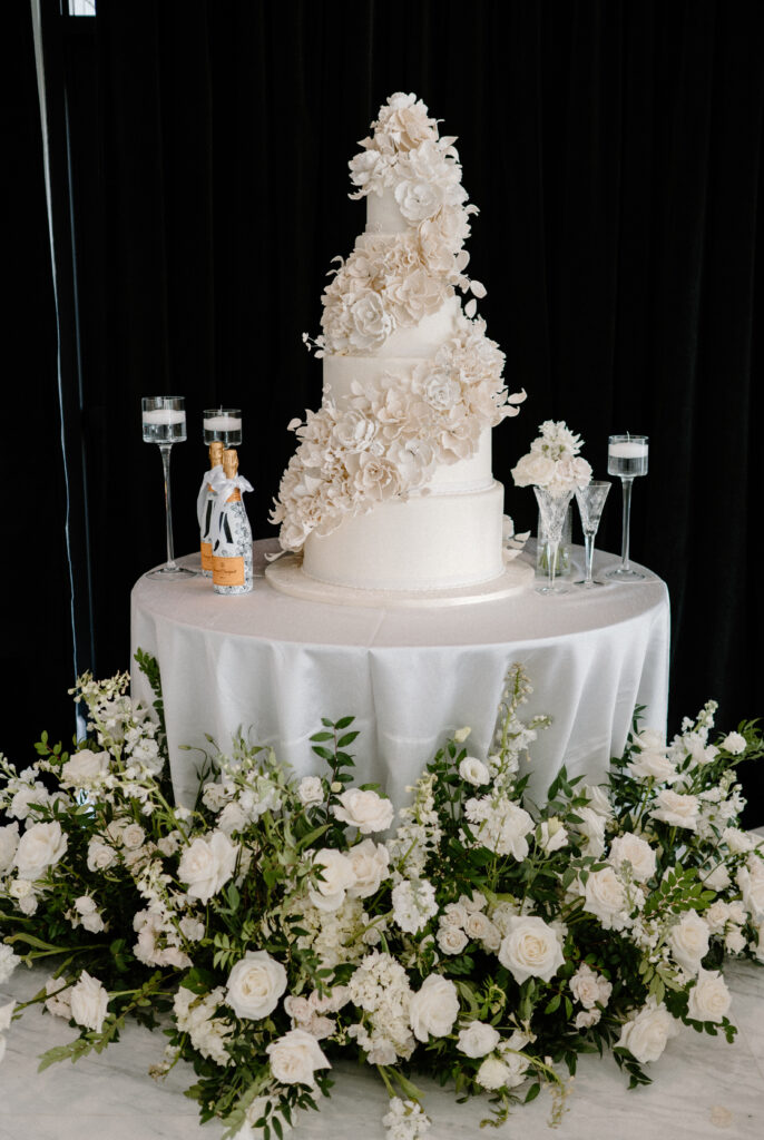 An elegant wedding cake table set up with floating candles and floral arrangements with greenery and white roses around the base of the table