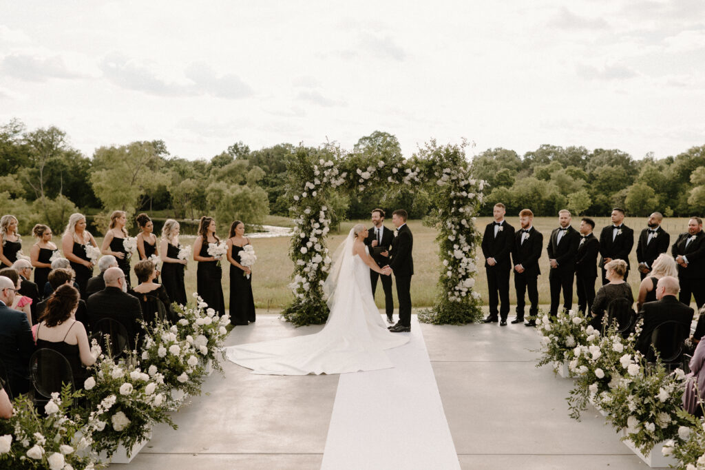 Bride and groom standing in front of the ceremony alter with a large square floral arch made with white roses and greenery