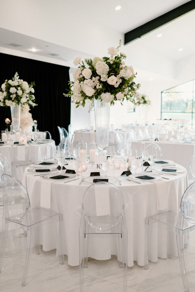 Wedding reception guest table with white linens and tall floral arrangements made with greenery and white flowers 