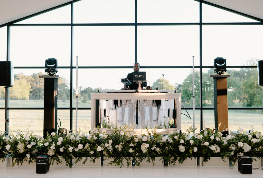 Large white facade boxes filled with greenery and white blooms placed in front of the stage for the wedding reception