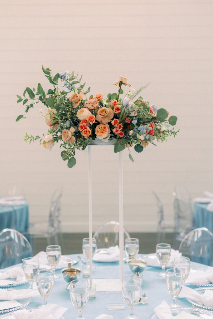 A large colorful flower arrangement placed on a white stand and sat on guests tables for a spring wedding reception