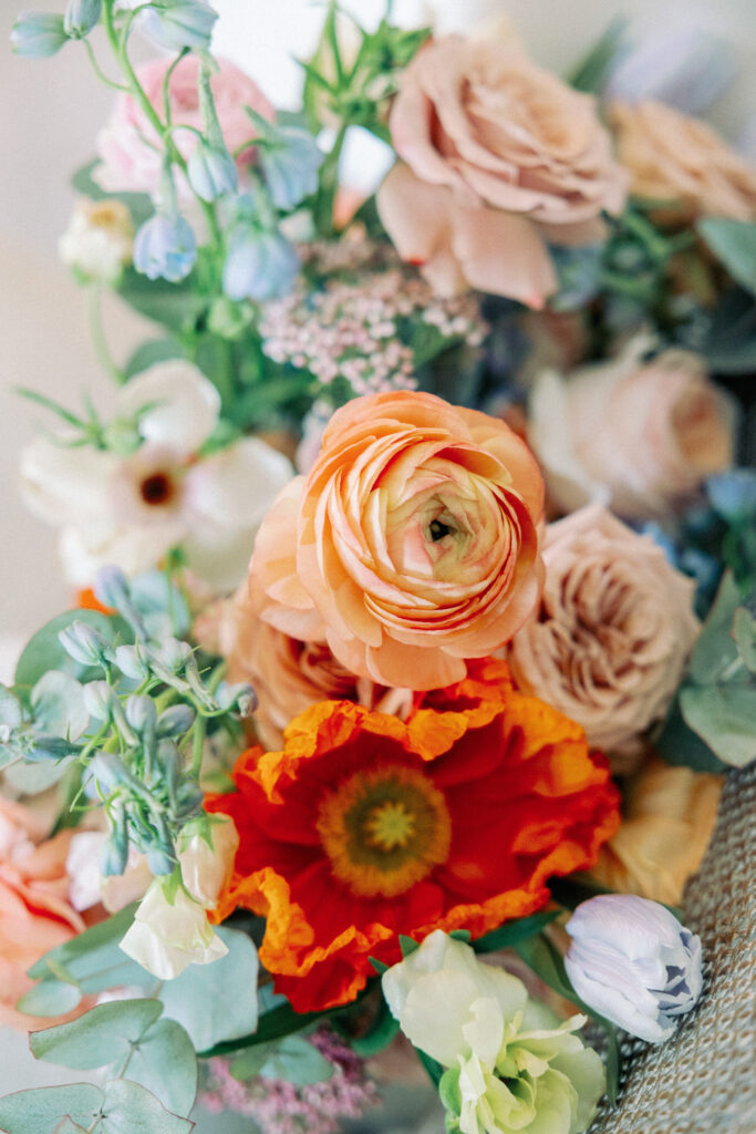 A spring bridal bouquet made  brightly colored flowers such as poppies, roses, tulips, and ranunculus 