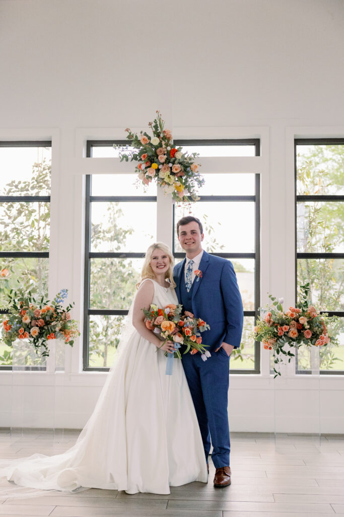 Bride and groom standing at the wedding ceremony alter with brightly colored flowers placed on the cross and beside them