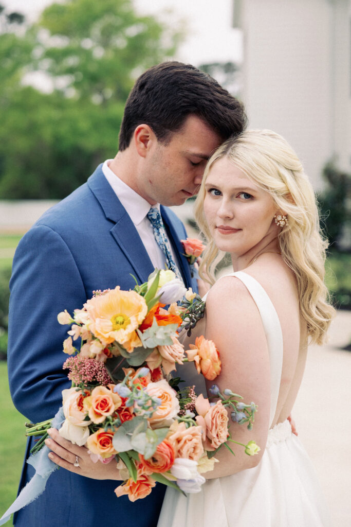 Bride and groom posing with bride's bouquet that is made with brightly colored spring blooms including poppies
