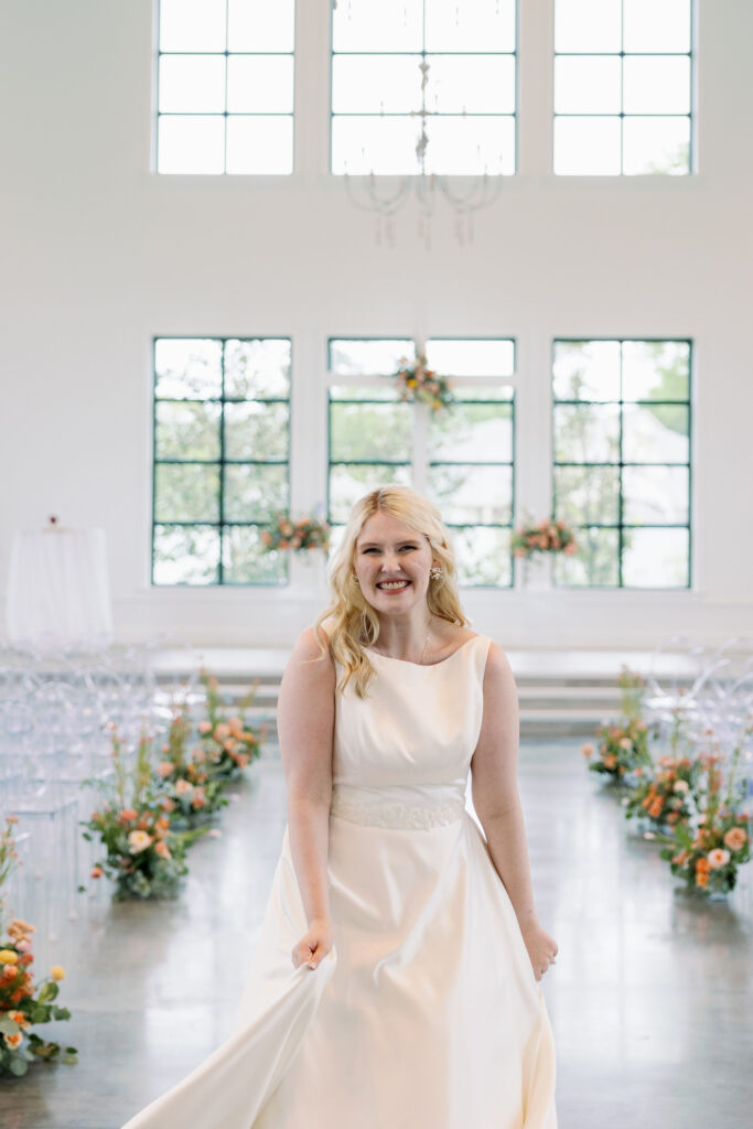 Bride standing in wedding ceremony site with brightly colored flowers running down the aisle and on the cross at the alter