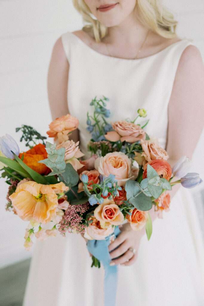 Bride posing with her brightly colored bouquet that includes poppies, roses, and tulips