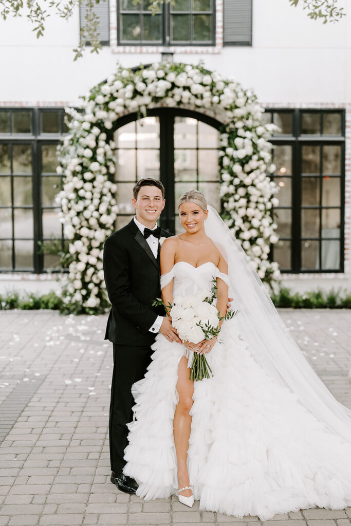 Bride and groom standing in front of their venue with a large and lush floral arch surrounding the entire entrance
