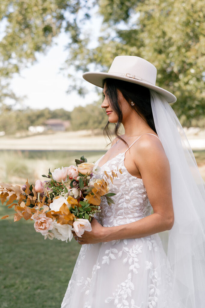 Modern fashionable bride wearing a hat posing with her bridal bouquet made with fall colored florals