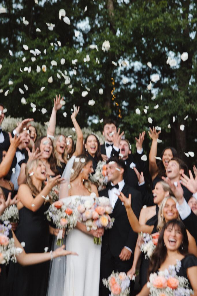 Wedding party posing while throwing rose petals in the air and holding bouquets made of baby's breath and pastel blooms