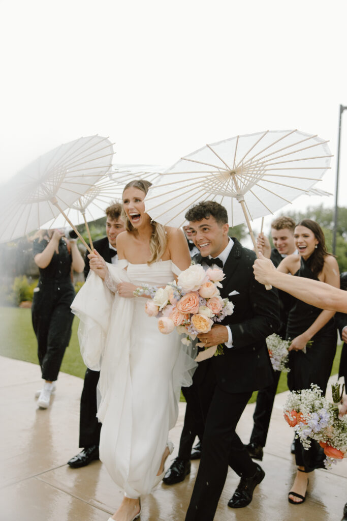 Bride and groom outside holding umbrellas and the brides pastel colored bouquet 