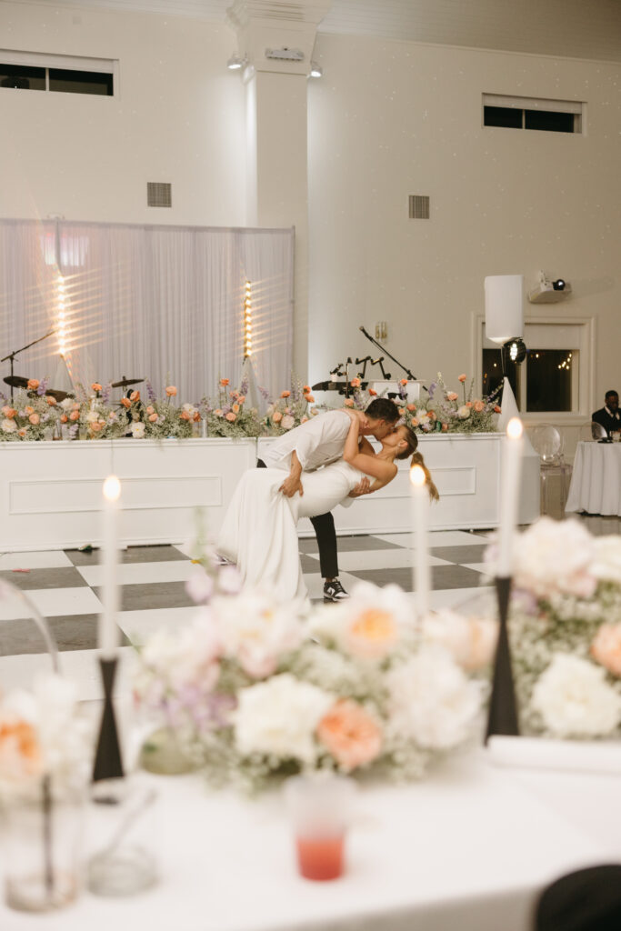 Bride and groom kissing while dancing in front of band stage lined with florals