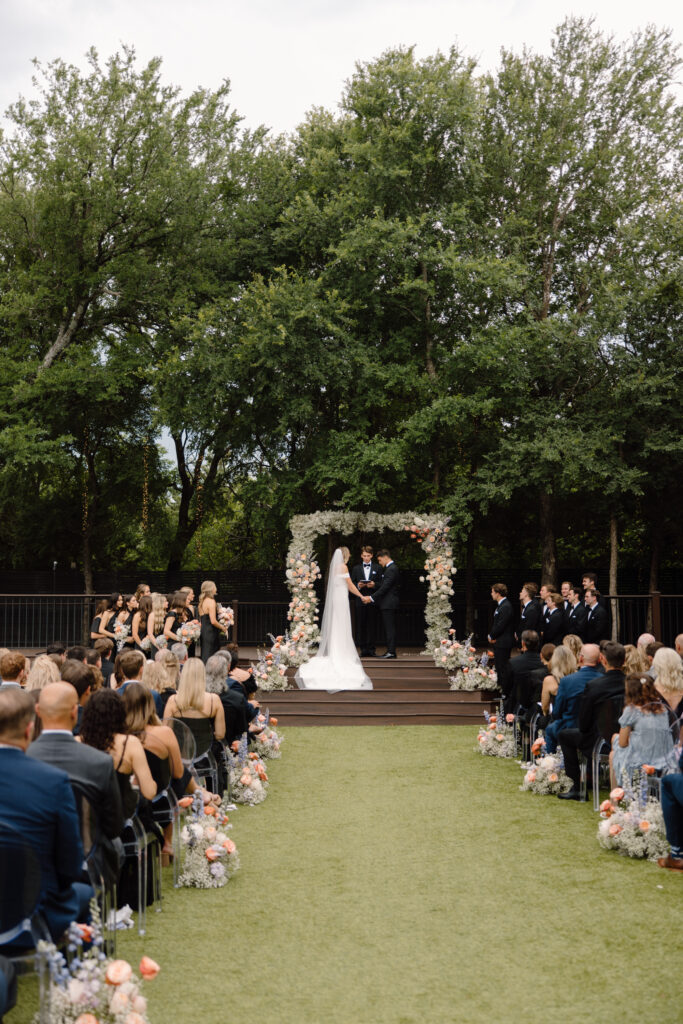 Modern floral arch made of baby's breath and pastel colored flowers with matching ground floral aisle markers