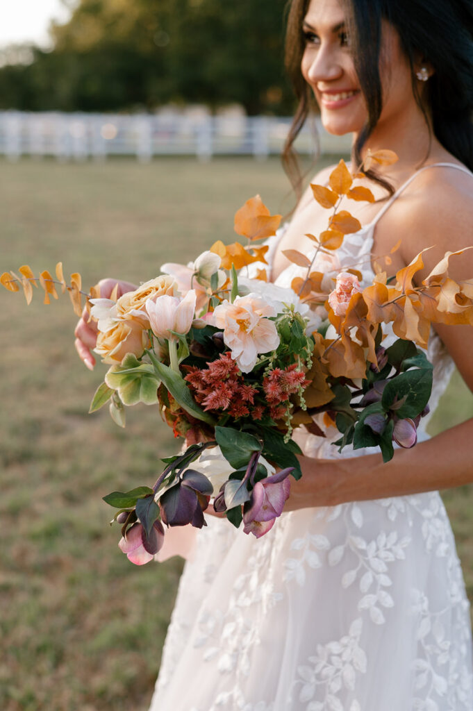 Bride posing with her bridal bouquet made with fall colored florals