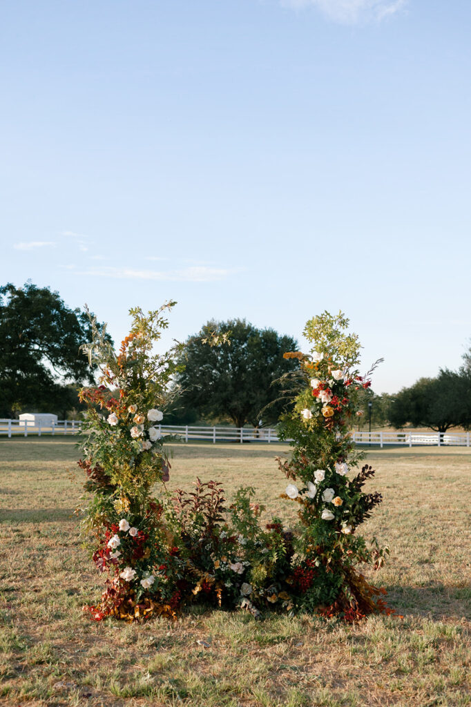 A lush broken arch installation for the wedding ceremony made with lots of organic greenery and fall inspired florals