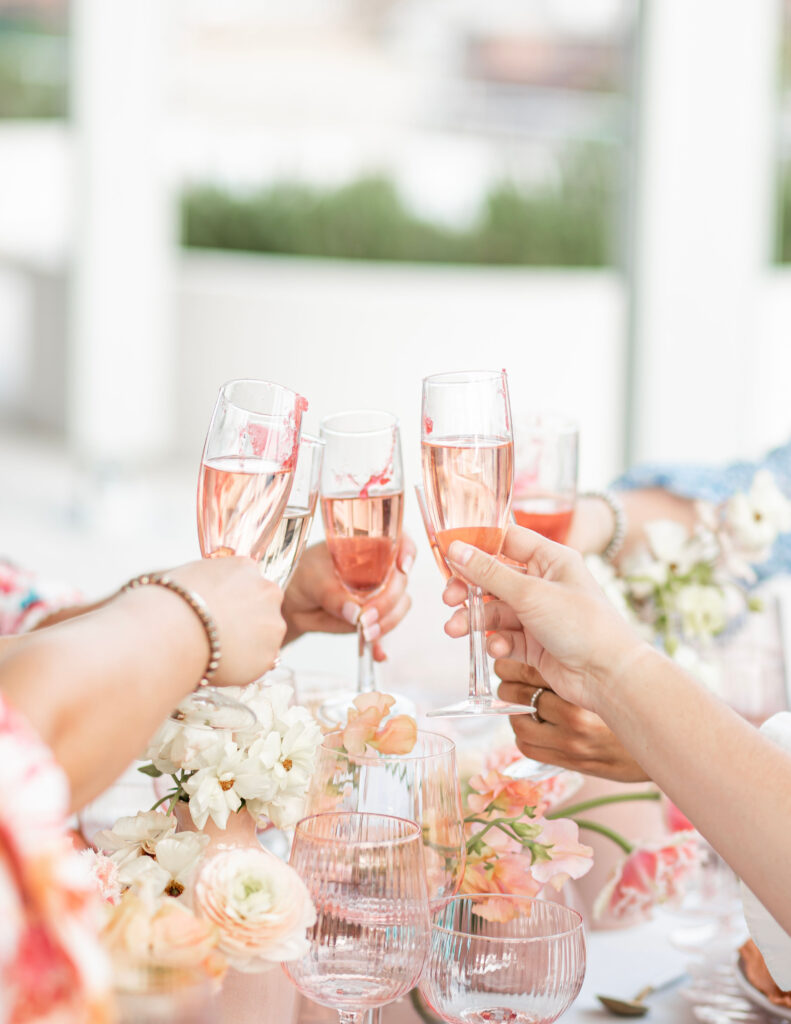 A champagne cheers at the bridal brunch with dainty pink and pastel colored flowers to set the table 
