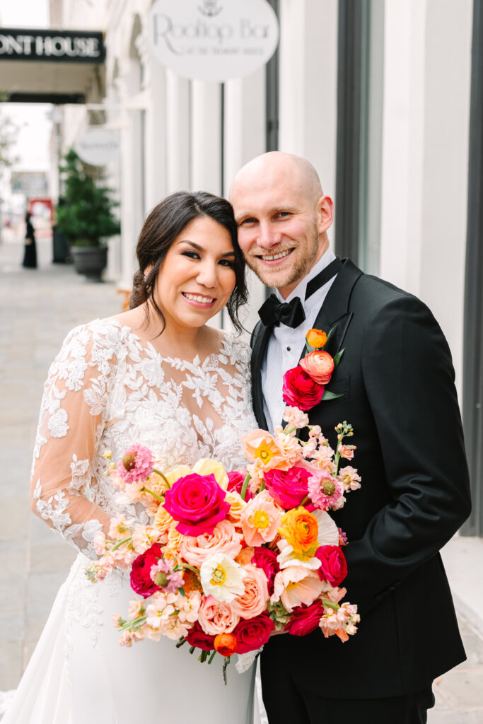 Bride and groom posing with the colorful bridal bouquet made with pink and orange flowers