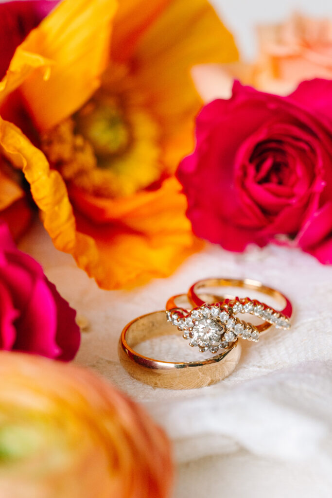 His and hers wedding rings placed next to colorful orange and pink blooms