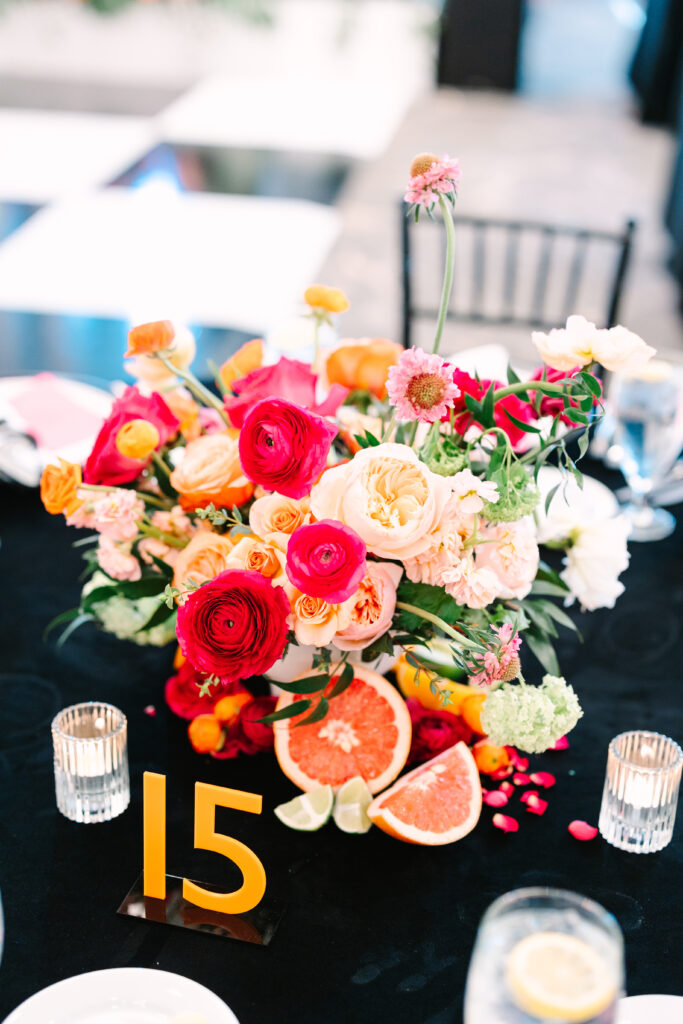 A colorful floral compote made with bright pink and orange flowers with accenting fruit placed at the base