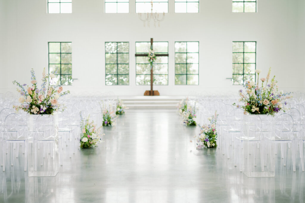 Ceremony aisle with ground floral arrangements in pastel colors with a matching arrangement on the cross at the alter