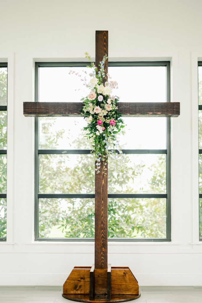 Textural pastel floral arrangement installed on wooden cross at ceremony alter