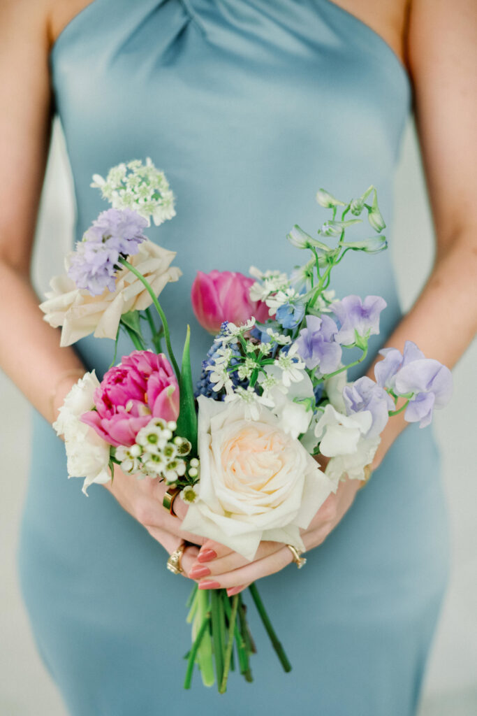 A whimsical pastel colored bouquet for spring wedding for the bridesmaid who is wearing a silk blue dress