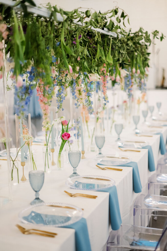 wedding reception table with hanging greenery and florals placed above the table and running the length of the table with bud vases of accenting florals placed on the table