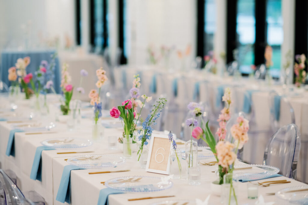 Blue taper candles with gold holders mixed with glass bud vases with pastel colored blooms placed on wedding reception table